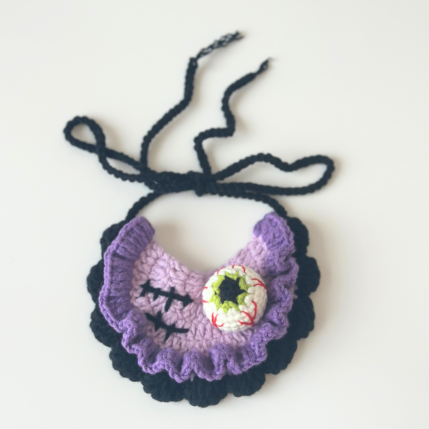 Crocheted purple bib with black straps on a white background