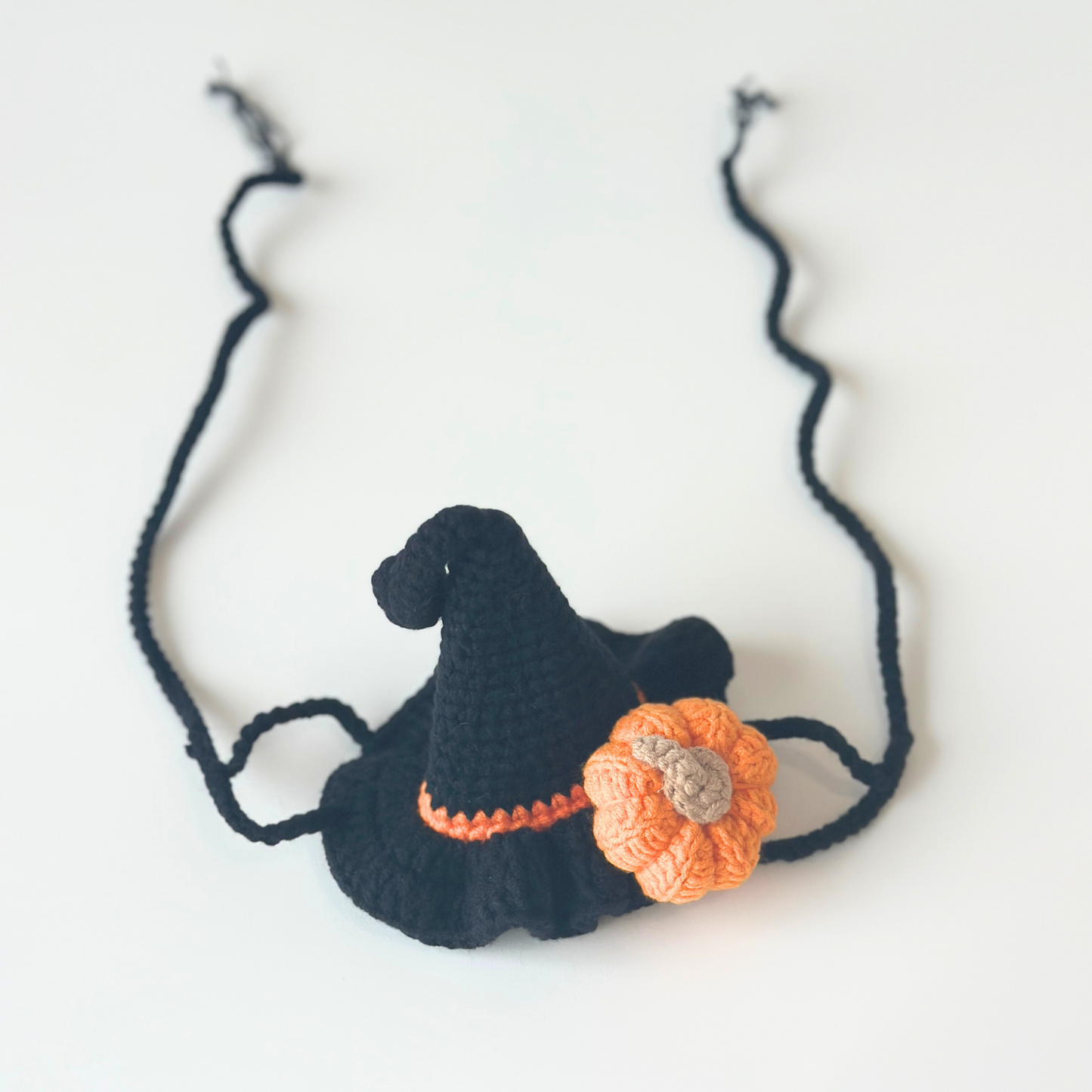 Crocheted witch hat with orange pumpkin and black straps on a white background