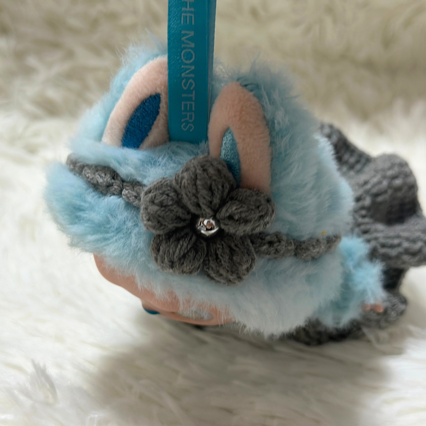 Labbubu doll wearing a fluffy blue fur coat with grey crocheted flower decoration and pearl center detail