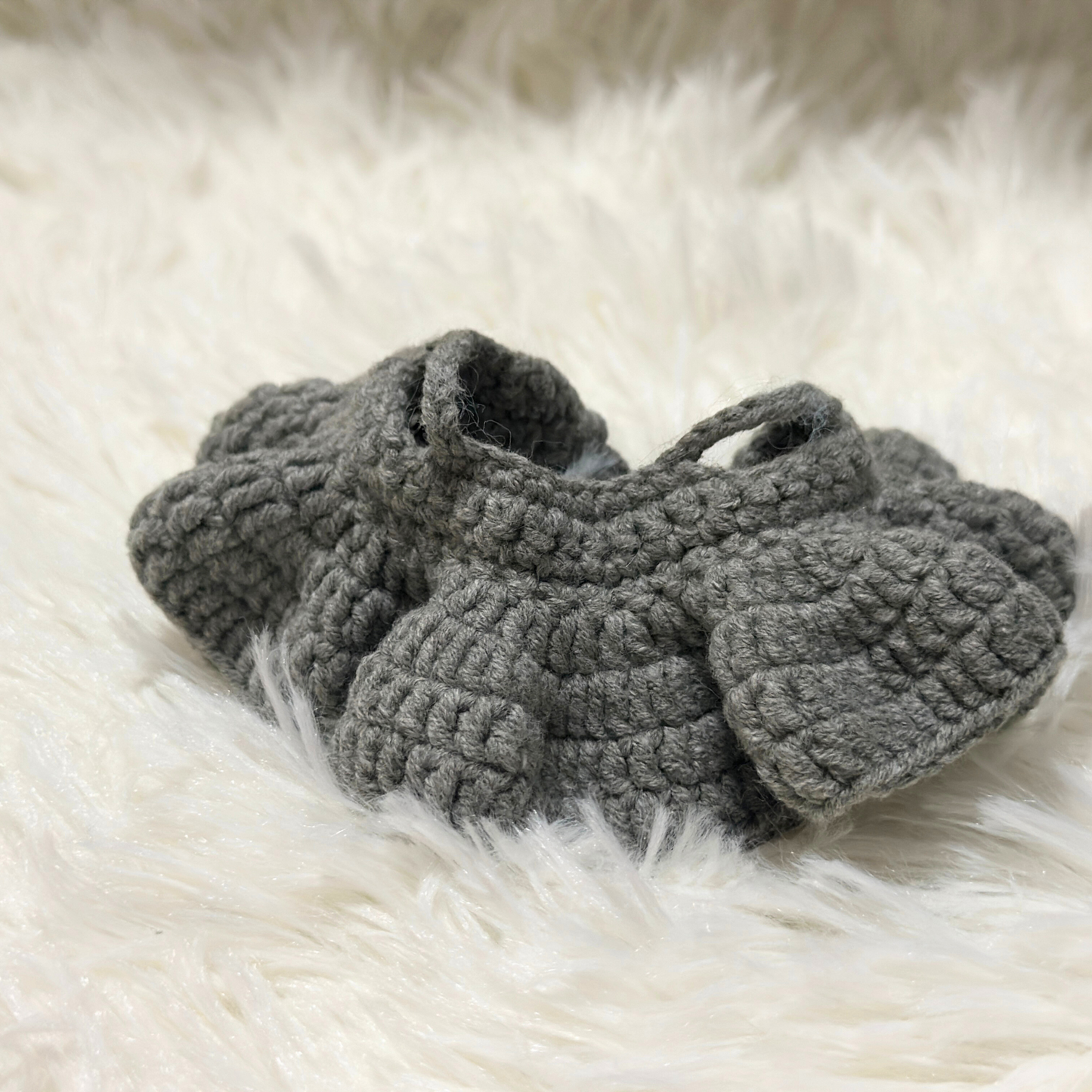 Close-up detail of grey crocheted Labbubu doll skirt showing intricate stitch patterns and fabric texture on white fur background