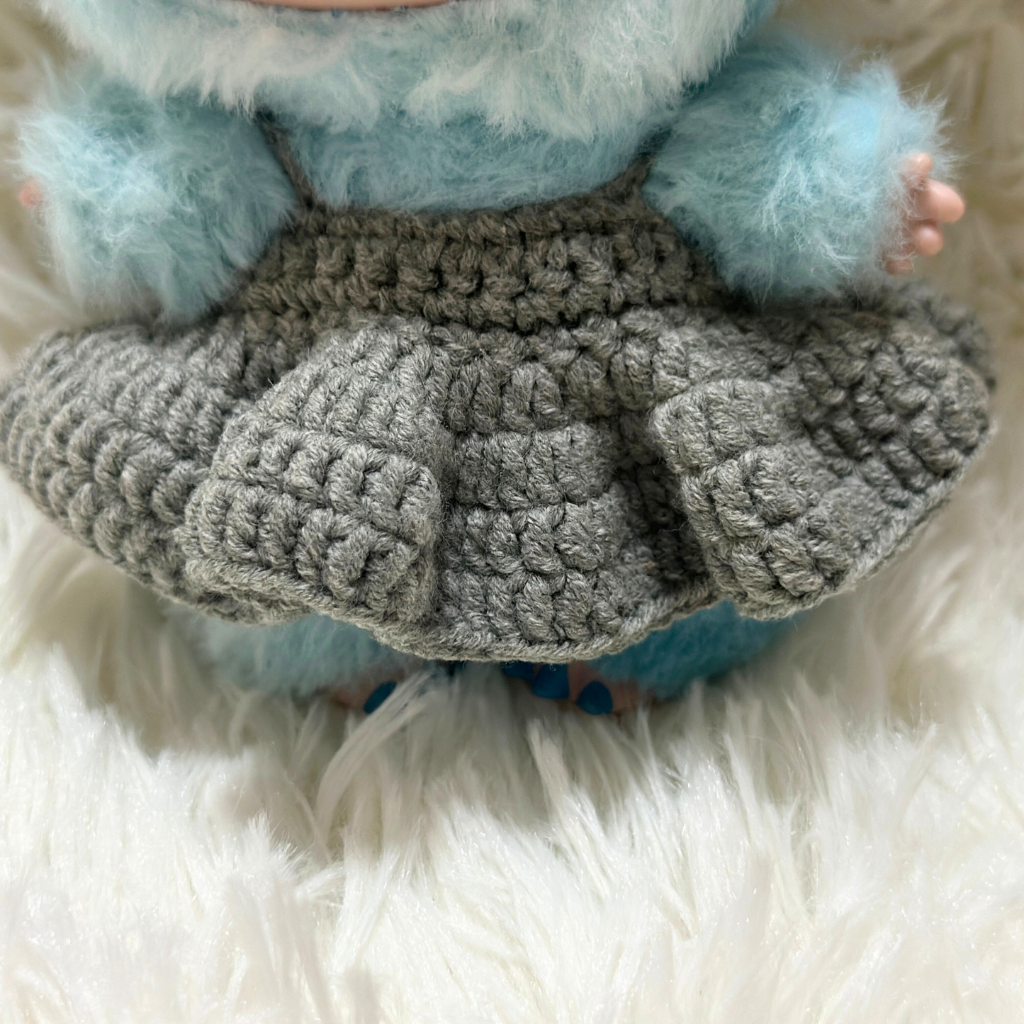 labubu wearing a gray knitted skirt on a white fluffy surface