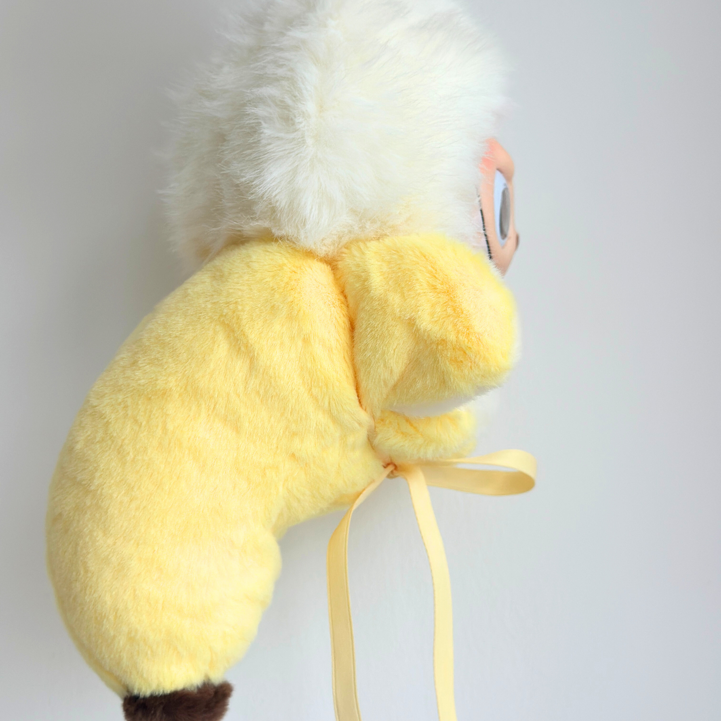 A cute Labub plush toy wearing a yellow banana costume with white fluffy hair and orange beak