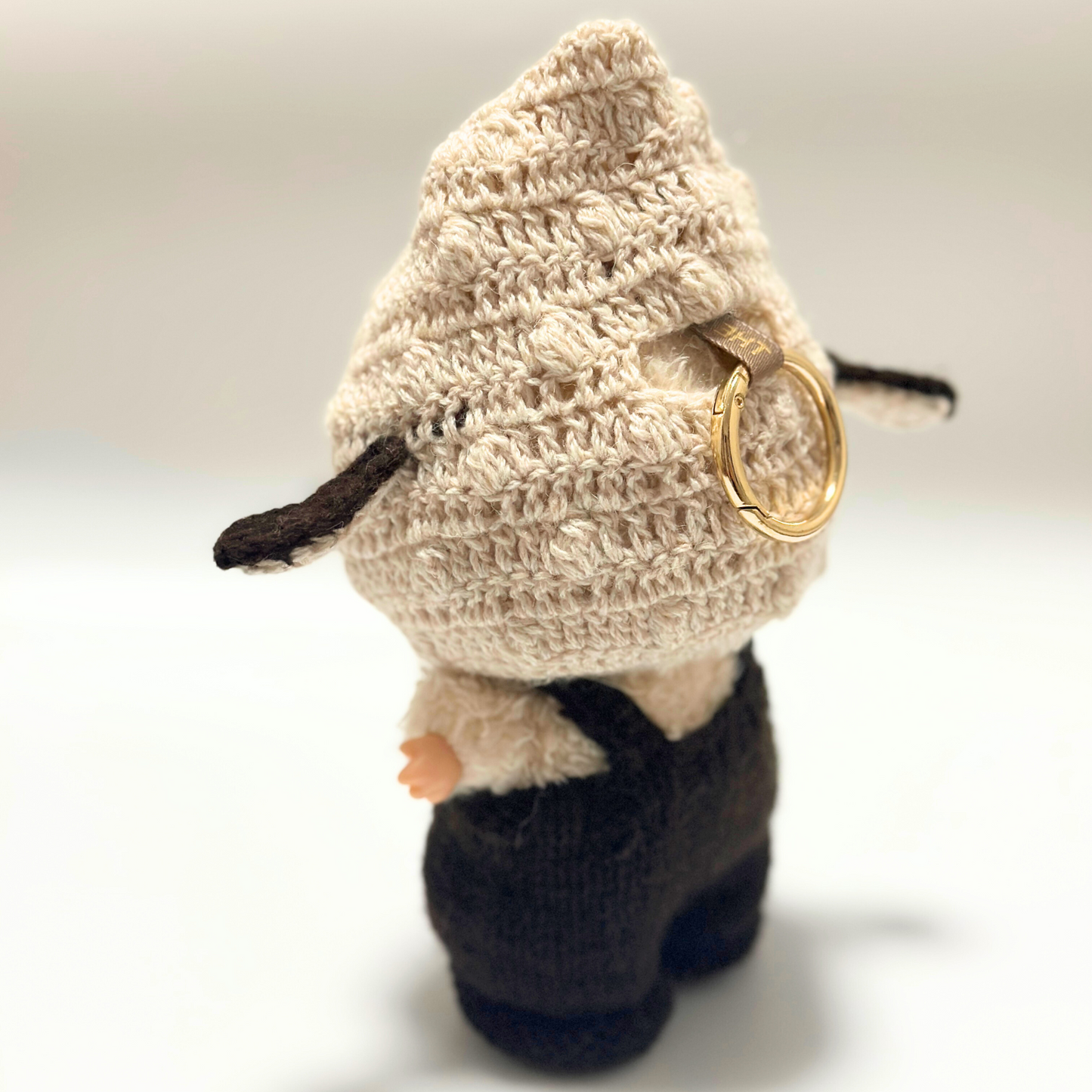 Back view of Labubu in cream knitted bunny ear hoodie and brown overalls showing detailed crochet texture and gold ring attachment