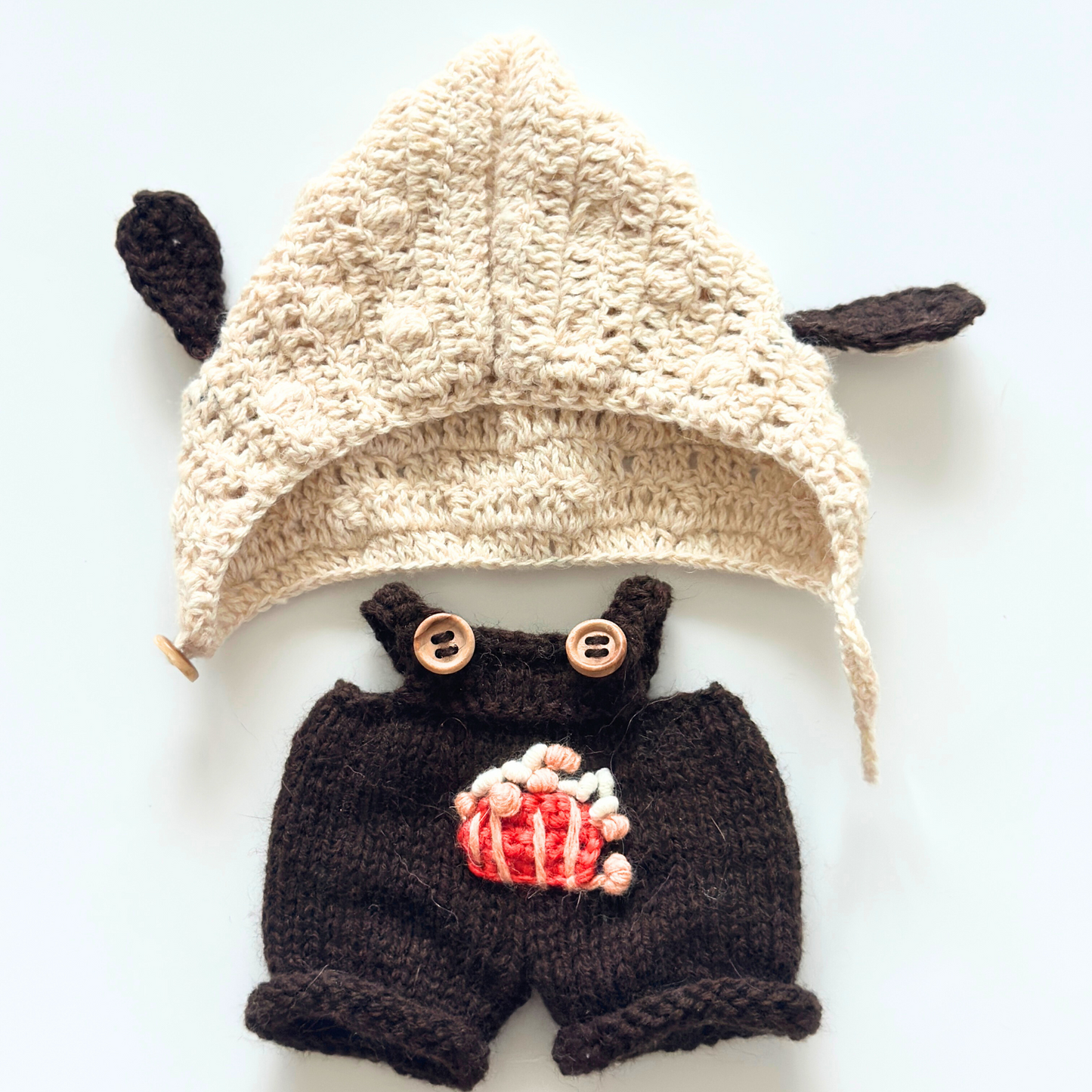 Flat lay of Labubu bunny ear hoodie and brown overalls clothing set showing cream knitted hoodie with ears and embroidered popcorn overalls with wooden buttons