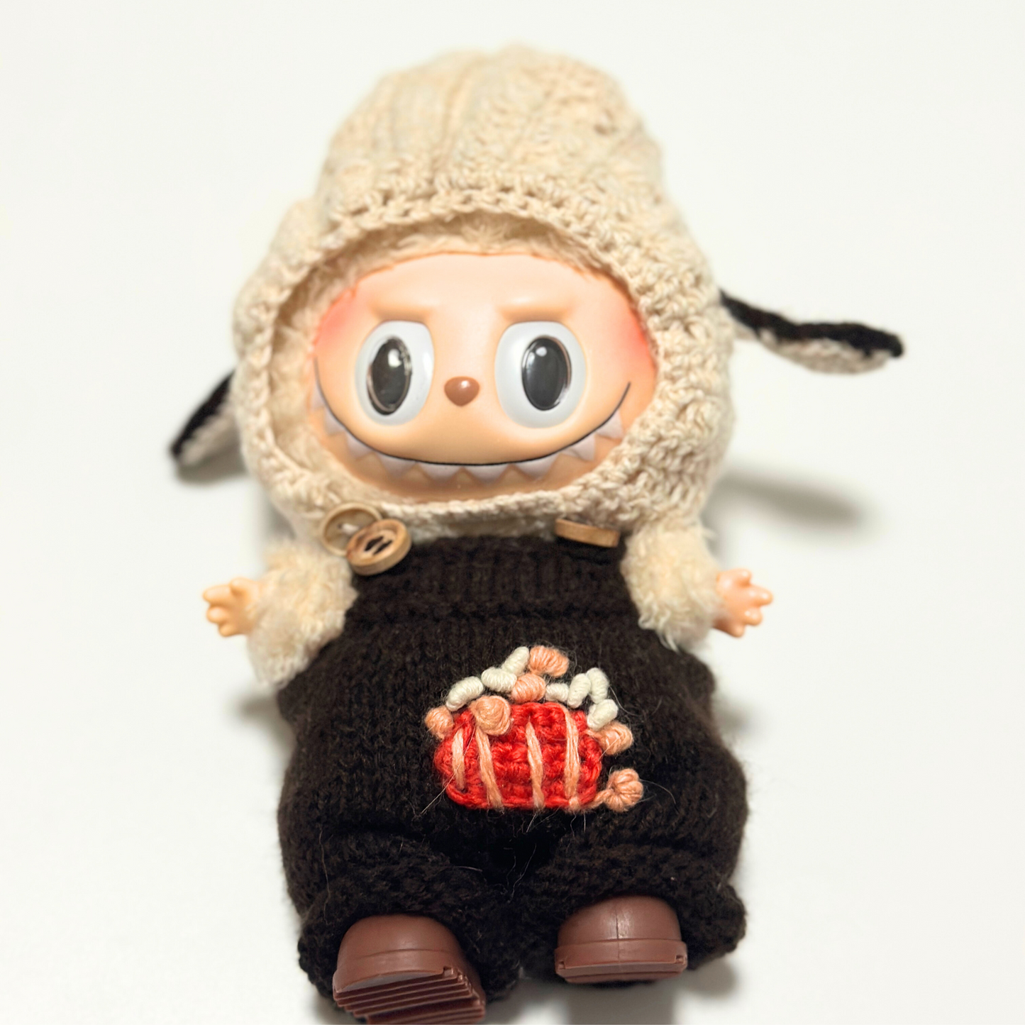 Labubu in cream knitted bunny ear hoodie and brown overalls with embroidered popcorn design - front view showing wooden button details