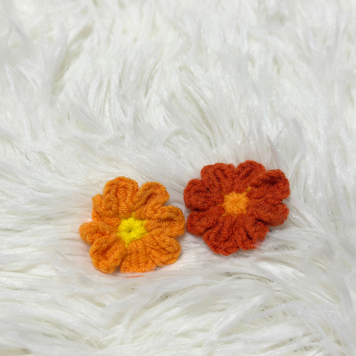 Two handmade crocheted flower accessories for Labubu dolls in orange and red with bright yellow centers, displayed on white fuzzy surface