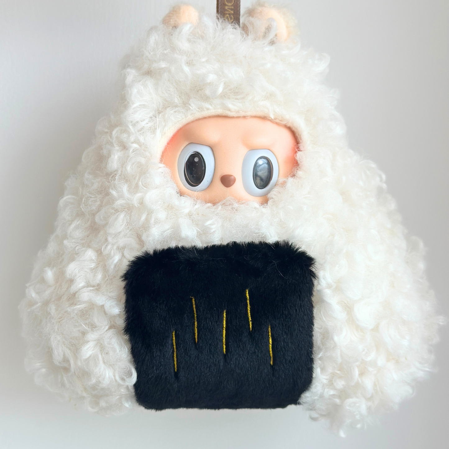 Labubu doll wearing nori (seaweed) onigiri costume with white fuzzy hoodie representing rice and black fuzzy bottom with yellow lines representing nori seaweed wrap - Japanese rice ball themed doll outfit