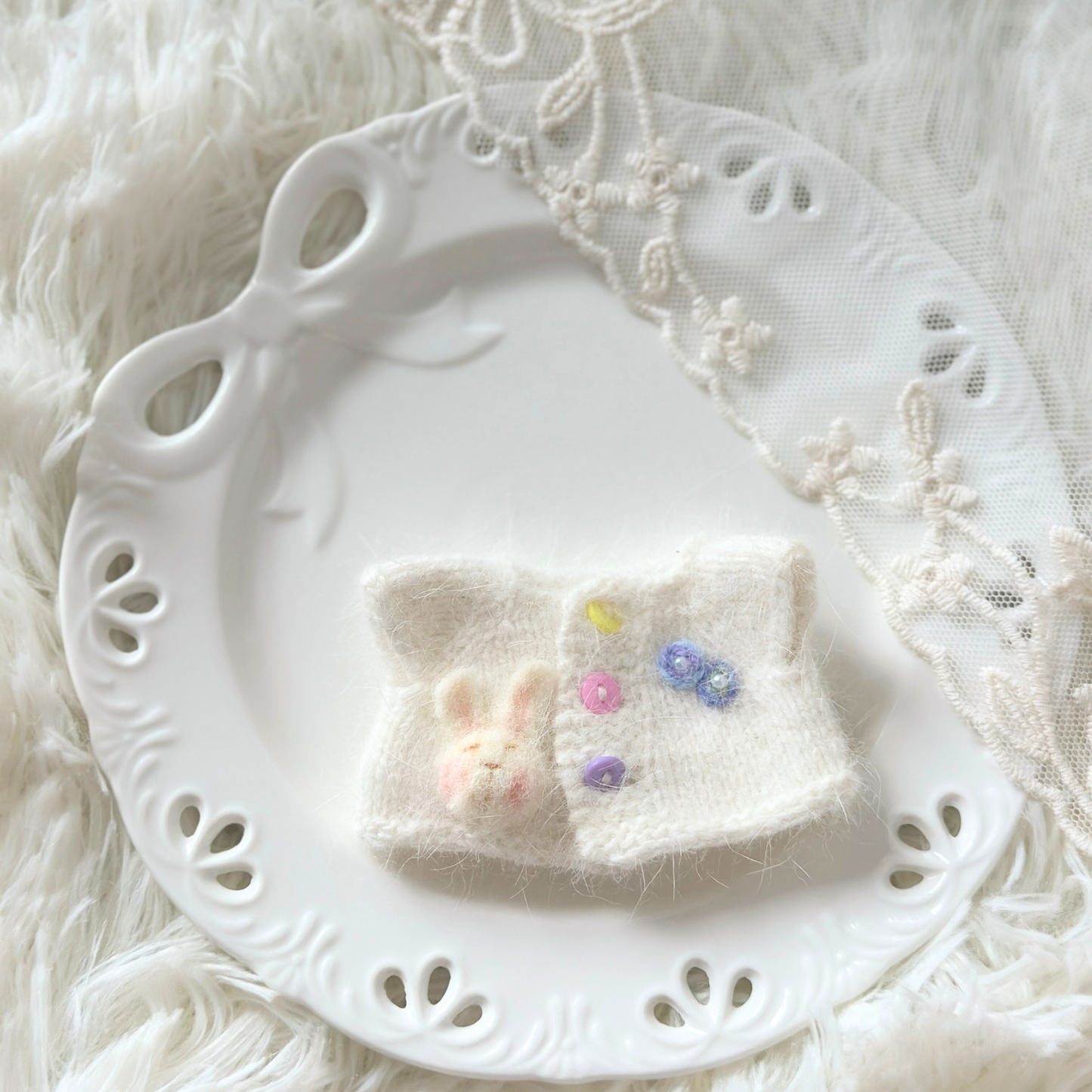 Small white knitted top with colorful buttons on a decorative white plate.