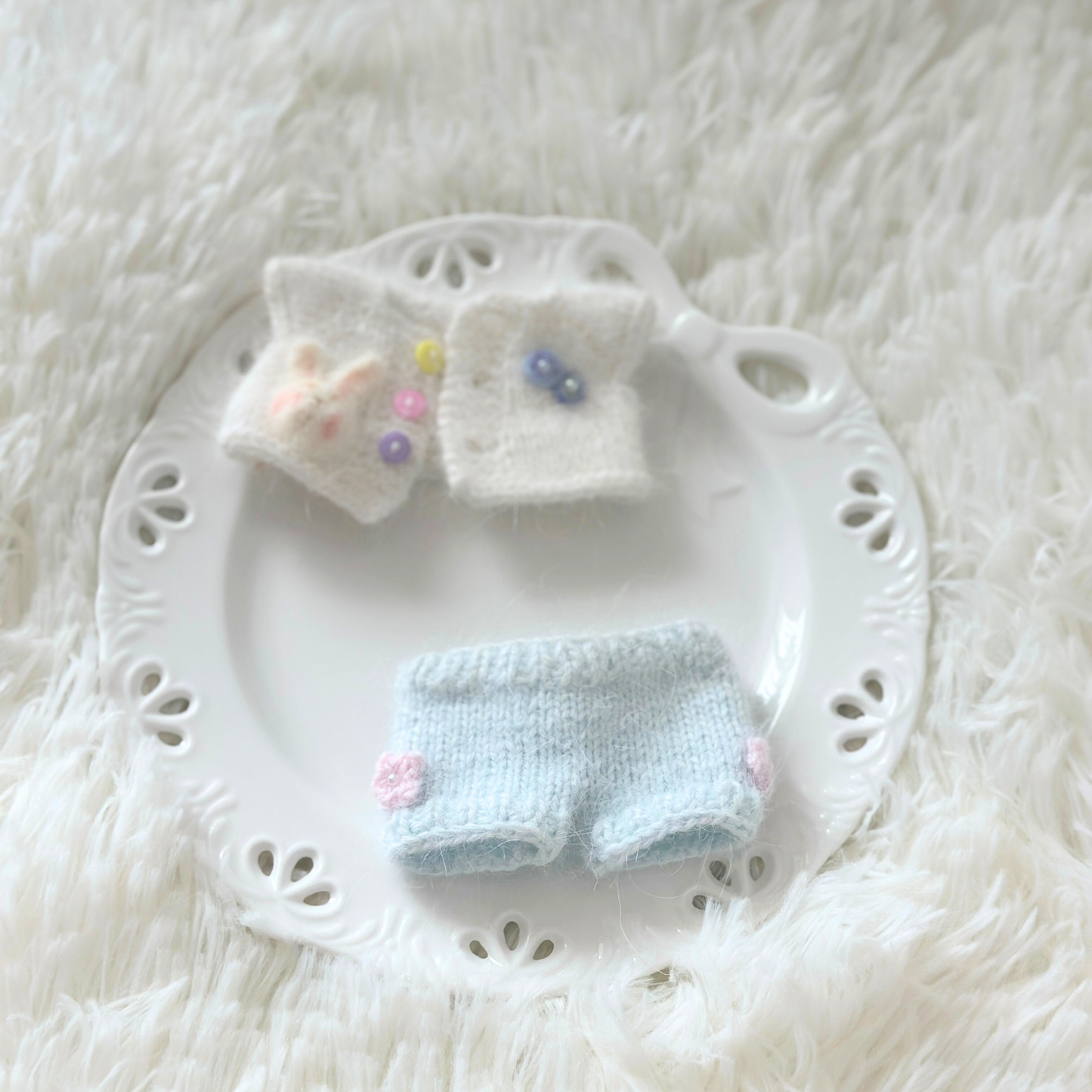 Knitted labubu outfit with top and pants on a white lace plate against a white textured background