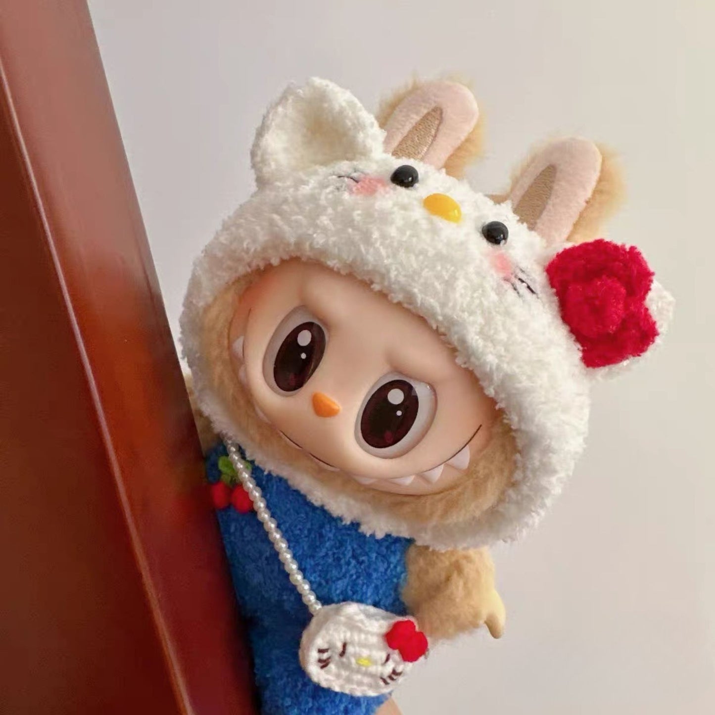 Labubu doll wearing a handmade Hello Kitty inspired outfit with fluffy white hood, red bow, and cute pearl bag