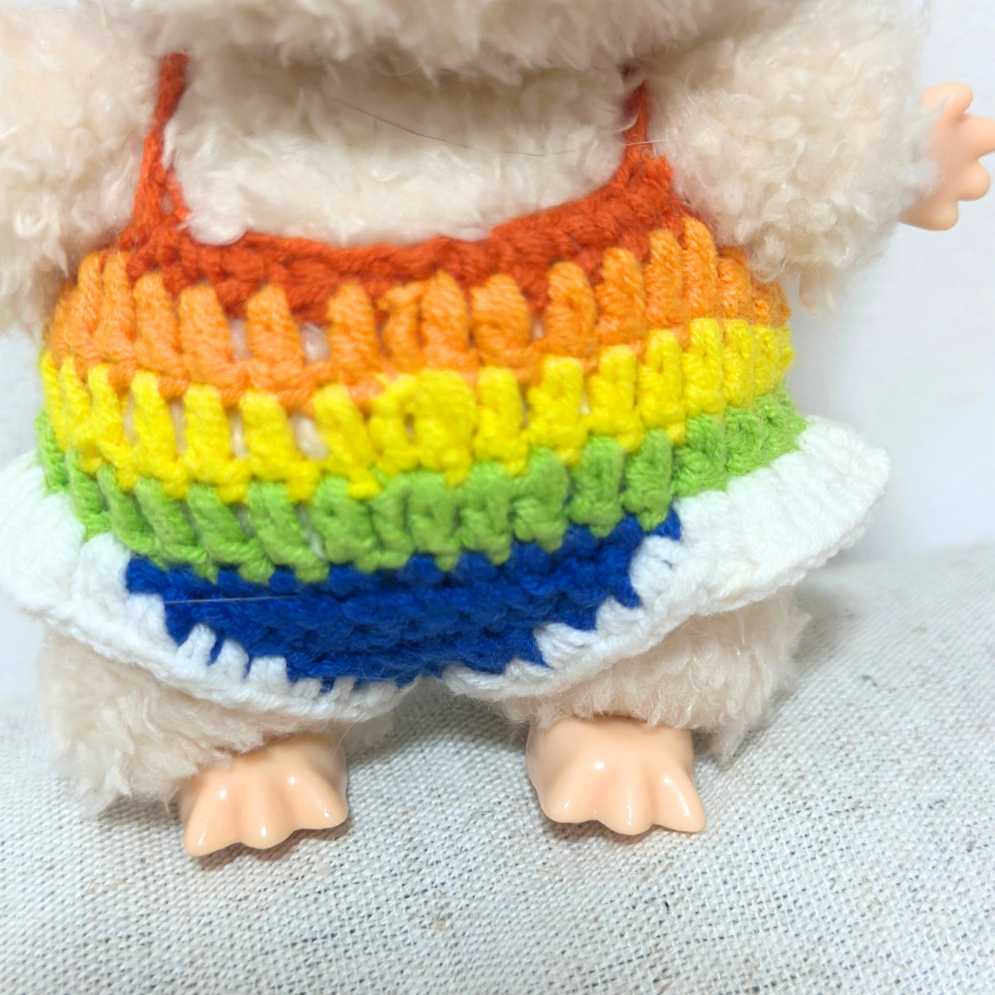 Close-up detail of Labubu's handmade rainbow gradient knitted dress showing intricate crochet stitching in red, orange, yellow, green, and blue stripes with white trim