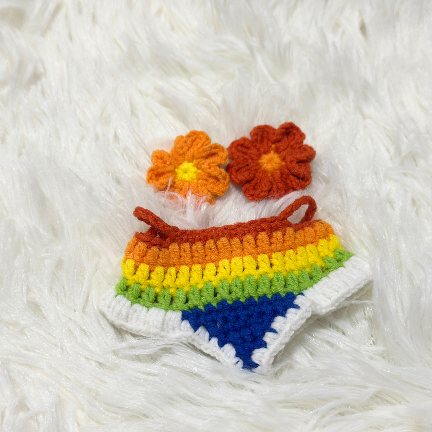 Complete handmade Labubu costume set laid flat on white fuzzy surface, featuring rainbow gradient crochet dress and matching orange and red crocheted flower accessories
