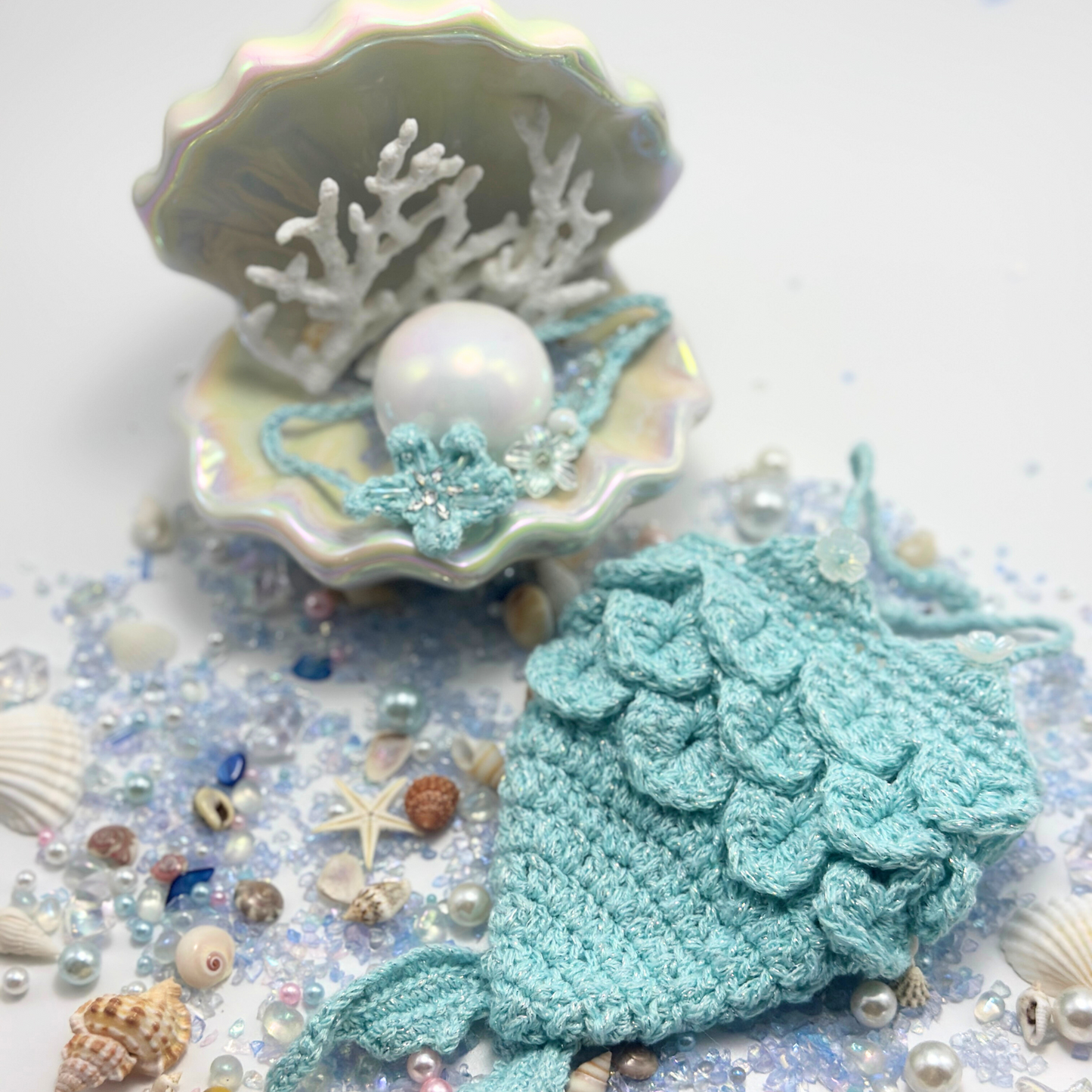 Empty Labubu mermaid costume in mint green crocheted scales displayed in magical ocean scene with iridescent shell containing white coral and pearl, surrounded by seashells, starfish, pearls and ocean treasures. Shows detailed scale texture and craftsmanship without doll, creating enchanting underwater fantasy display perfect for showcasing collectible mermaid costume quality.