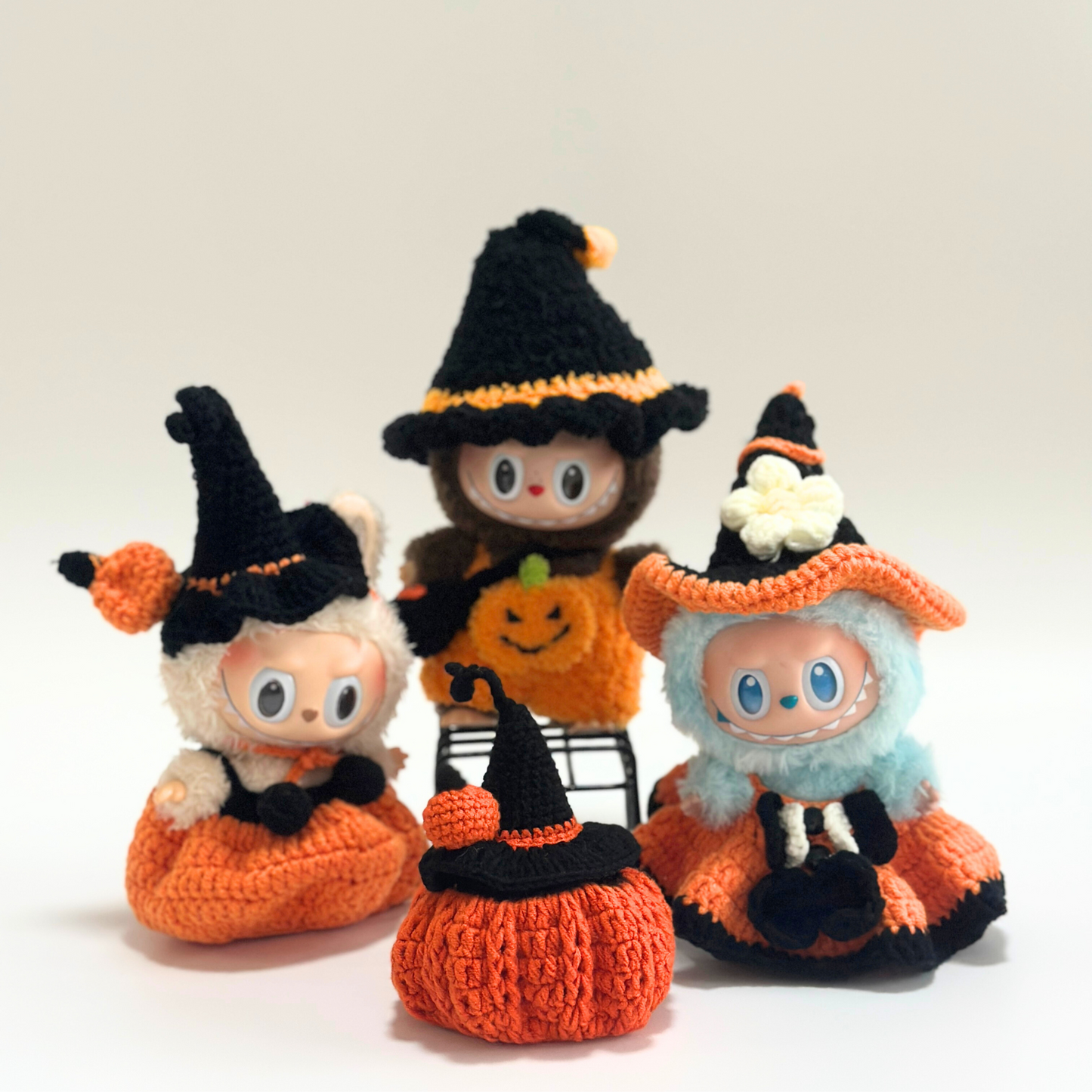Group photo of handmade crocheted Halloween costumes for Labubu dolls featuring multiple themed outfits: witch costumes with black hats and orange pumpkin jumpsuits, orange pumpkin-shaped standalone costume with witch hat, and various Halloween accessories including trick-or-treat bags. Complete Halloween doll costume collection, seasonal miniature clothing set, collectible toy accessories for Halloween enthusiasts and craft lovers.