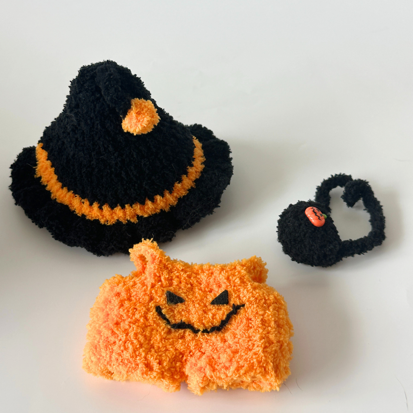Complete handmade crocheted Halloween costume set for Labubu doll laid out showing all components: black witch hat with orange pom-pom and trim, orange textured pumpkin jumpsuit with embroidered jack-o'-lantern face, and black crocheted trick-or-treat bag with orange pumpkin charm. Premium doll costume accessories, collectible Halloween miniatures, DIY crochet craft set for doll enthusiasts.