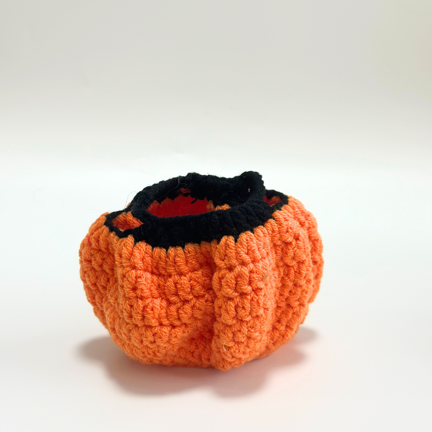 Interior view of handmade crocheted Halloween pumpkin costume body for Labubu doll without witch hat, showing orange textured pumpkin shape with ribbed crochet pattern, black rim detail, and red interior lining. Empty costume displays construction quality and dimensional pumpkin form, perfect collectible Halloween doll outfit for craft enthusiasts