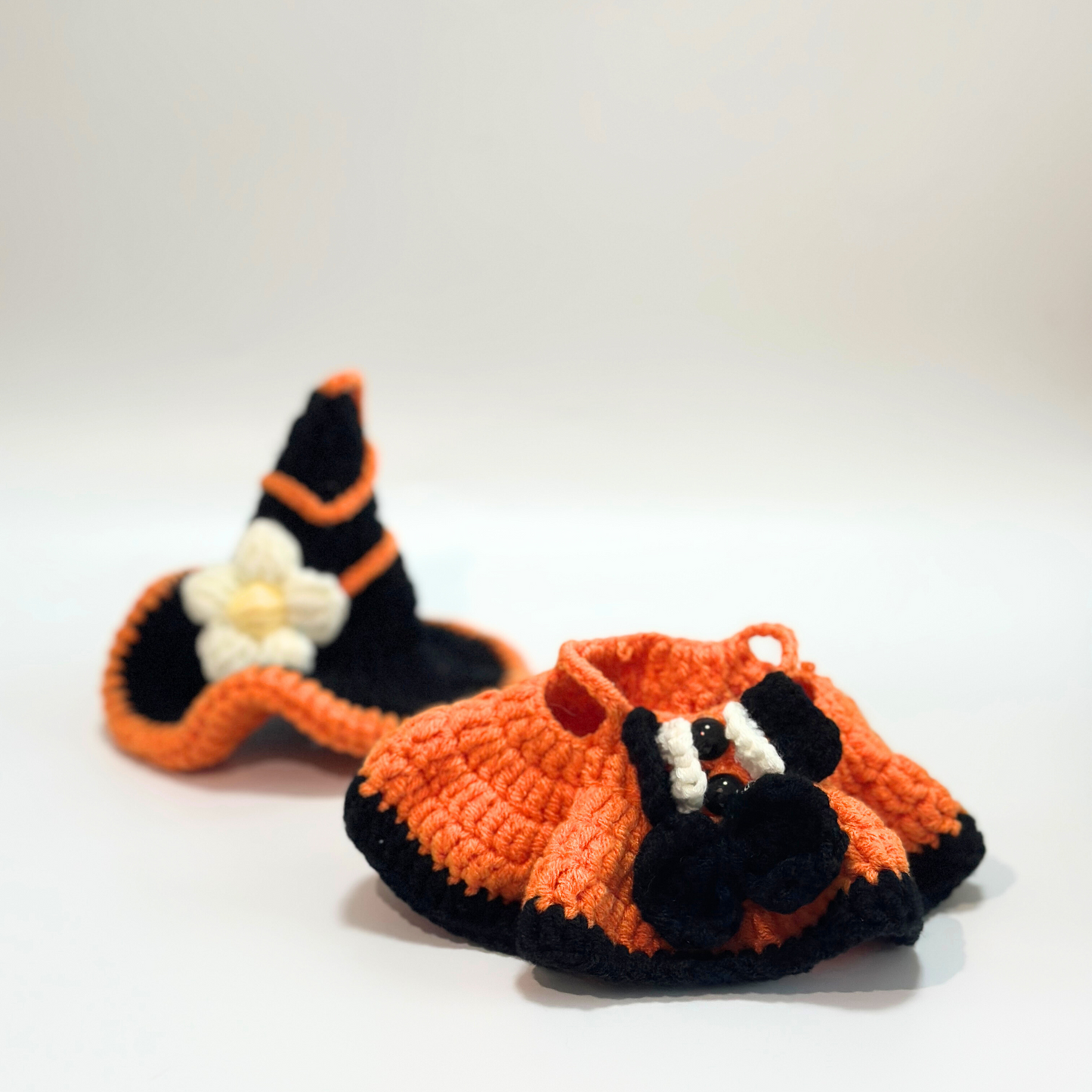 Flat lay view of handmade crocheted Halloween witch costume components for Labubu doll including black witch hat with orange trim and white daisy flower decoration, orange textured dress with black trim details, white accent straps, and drawstring closure. Shows individual costume pieces and quality construction details, perfect collectible Halloween doll accessories for craft enthusiasts.