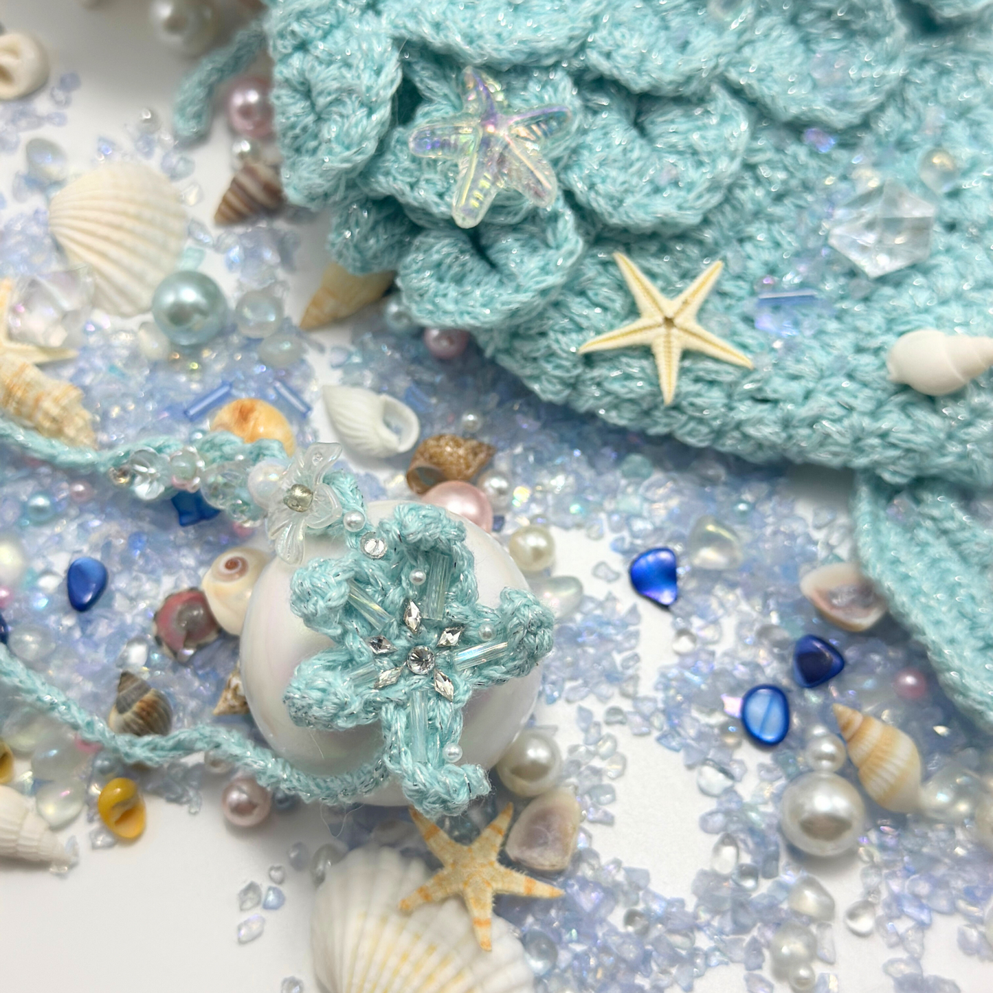 Close-up detail of Labubu mermaid costume crown featuring mint green crocheted headpiece with sparkly beaded decorations, iridescent starfish embellishments, surrounded by ocean treasures including pearls, seashells, blue gems, and golden starfish. Shows intricate craftsmanship of mermaid crown accessory with dimensional beadwork and sea-themed decorations, perfect collectible fantasy costume detail.