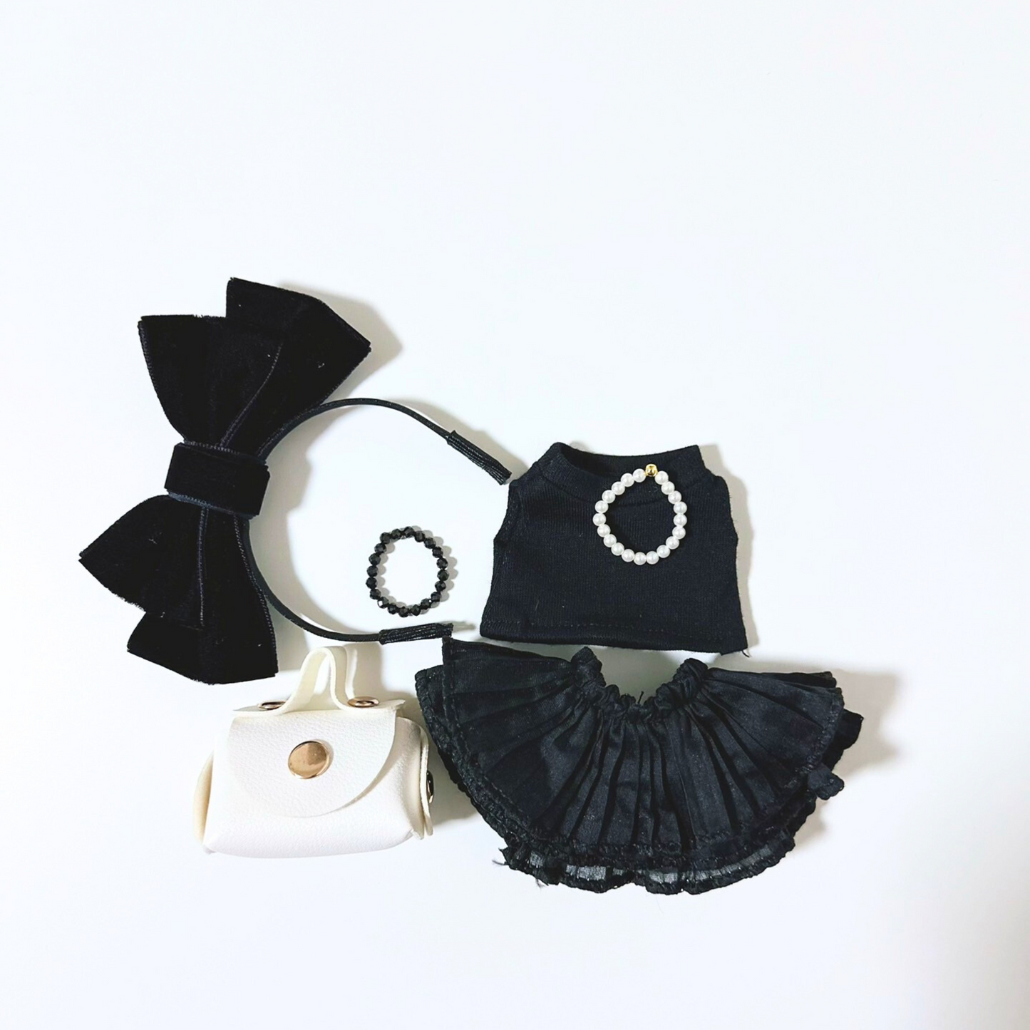 Molly doll accessories laid out separately including a black bow headband, black sleeveless top with white pearl circle detail, black ruffled lace skirt, white hand