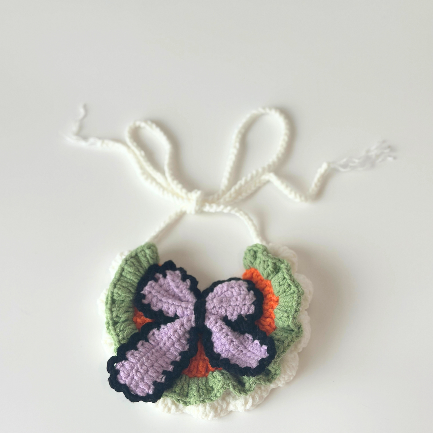 Crocheted butterfly with green wings and a purple body on a white background