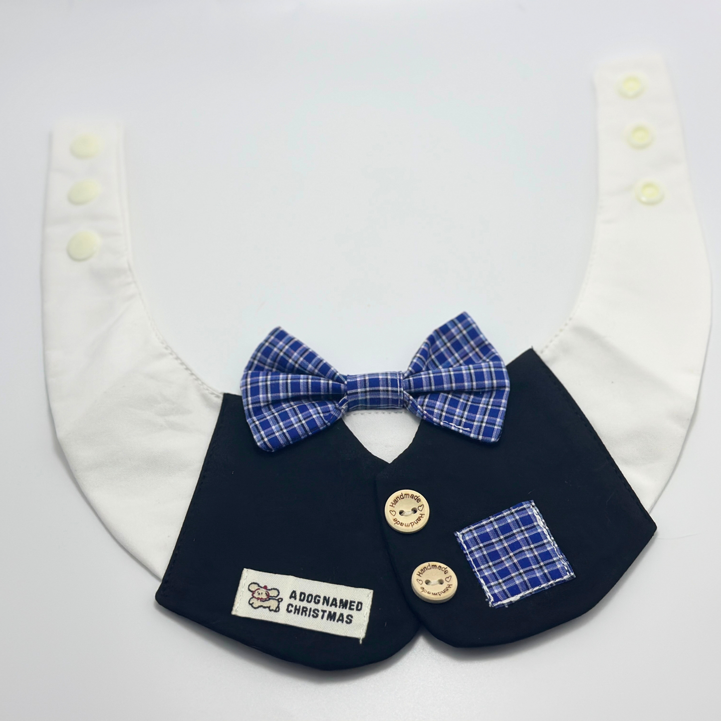 Navy blue pet bib with white collar, blue plaid bow tie, wooden buttons, and "A Dog Named Christmas" text label - formal dog bandana accessory