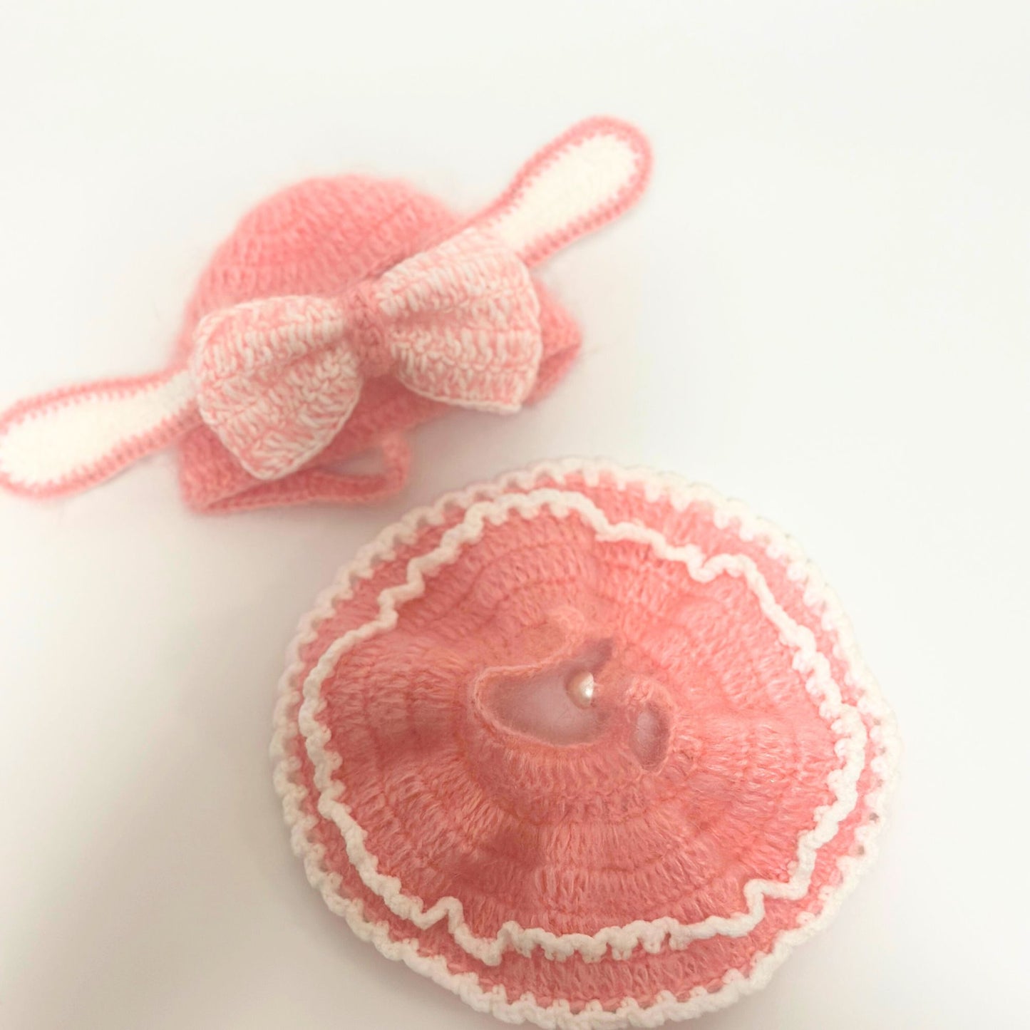 Two-piece handmade knitted bunny costume set for Labubu doll displayed separately on white background. Top shows pink rabbit ears headband with white bow detail. Bottom shows matching pink layered dress with white ruffled trim edges and button closure. Soft coral pink knitted fabric with white accent details.