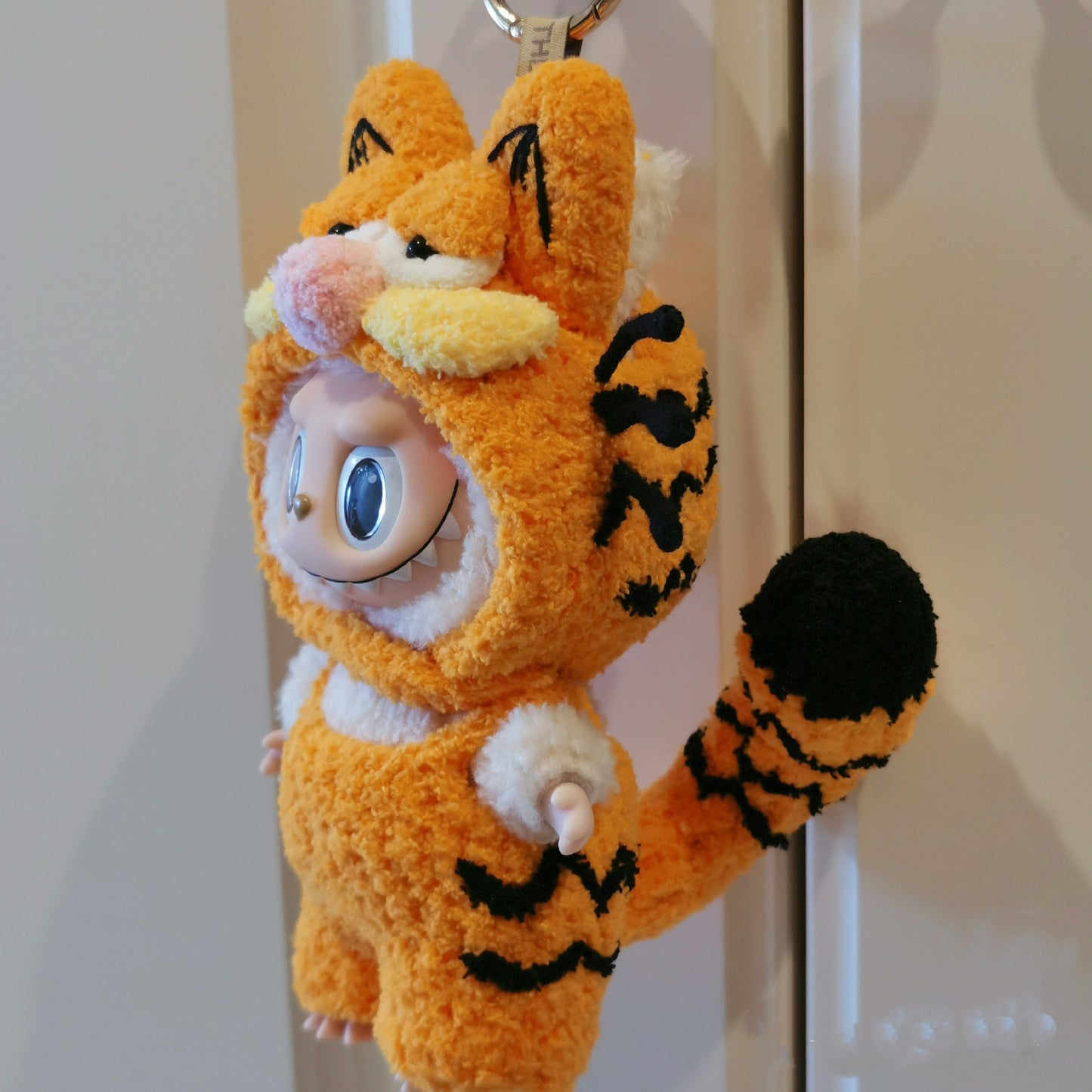 Labubu doll wearing a handmade Garfield-style orange plush outfit with cat ears and whiskers, cute fluffy costume inspired by Garfield