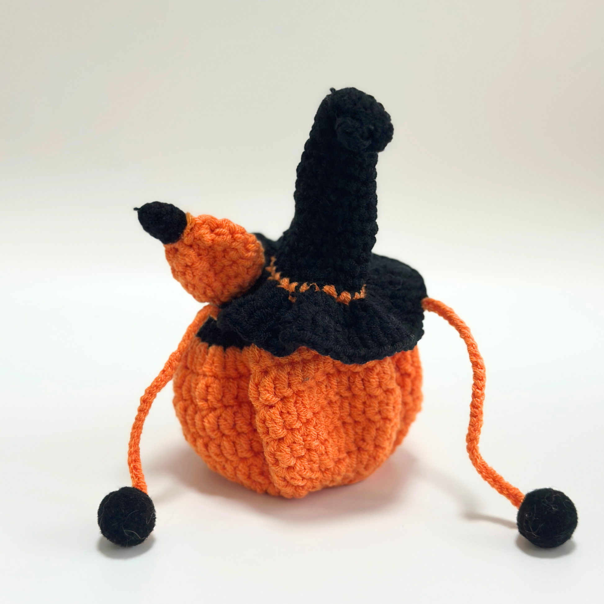Empty handmade crocheted Halloween pumpkin costume for Labubu doll displayed without doll inside, showing black witch hat with orange trim and pom-pom, orange textured pumpkin-shaped body with drawstring closure and black pom-pom ties. Perfect standalone Halloween doll costume, collectible seasonal craft item for toy enthusiasts and doll collectors.