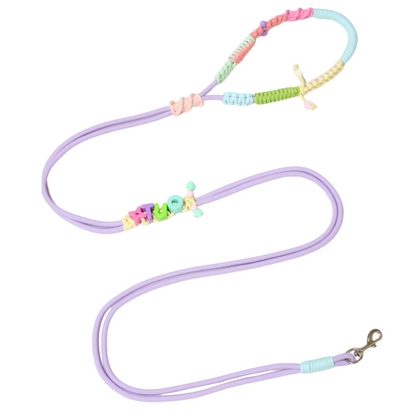 Custom handmade dog leash in pastel purple with personalized name 'HUGO' spelled in colorful letter beads, featuring rainbow macrame handle and adjustable design