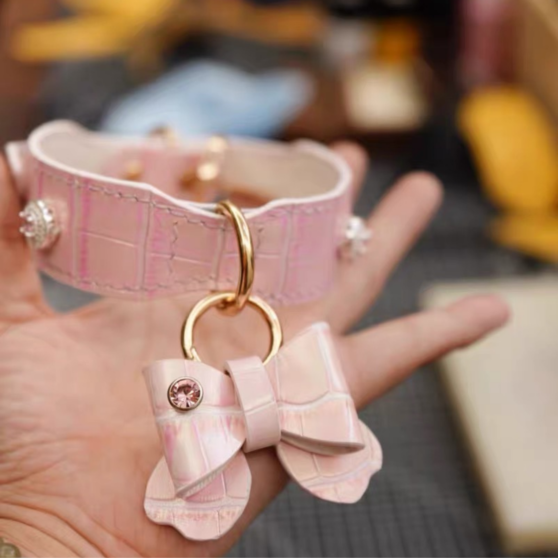 Pink crocodile-patterned dog collar with a bow-shaped charm held in a hand.