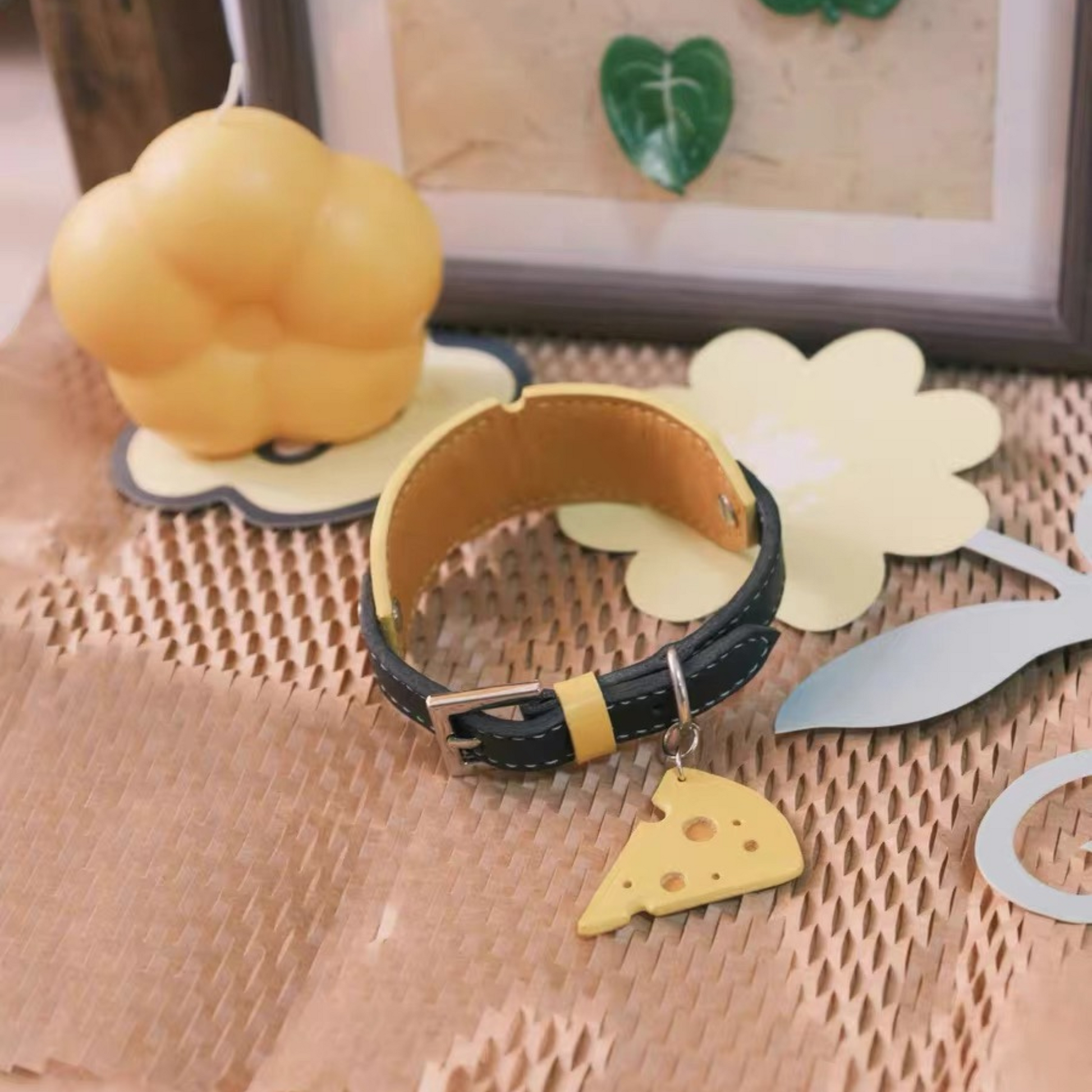 Handmade leather dog collar featuring cheese-shaped ID tag, styled with chef hat candle and paper decorations on textured surface