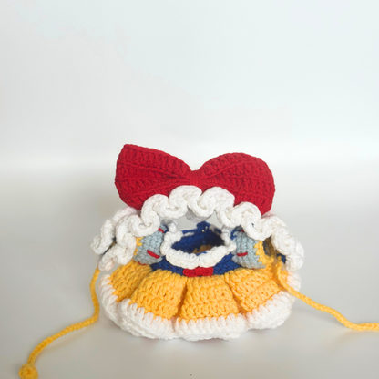 Front view of a crocheted Snow White costume for Labubu doll without the doll inside, showing the red bow headband at top, white ruffled bonnet trim, blue bodice with white collar and red accents, layered yellow ruffled skirt, white base, and yellow drawstring ties. The empty costume displays the intricate crochet construction and dimensional details of each component.