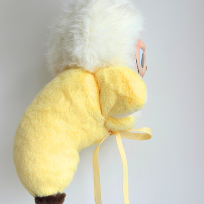 A cute Labub plush toy wearing a yellow banana costume with white fluffy hair and orange beak