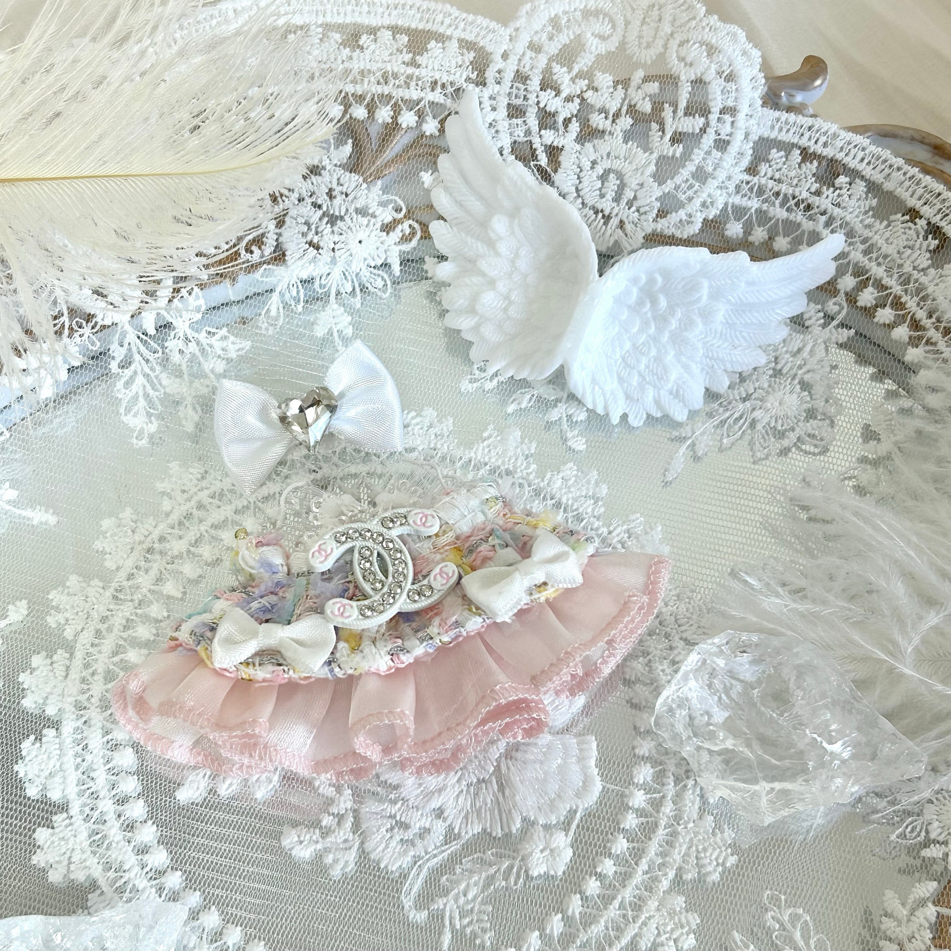 A delicate labubu 4.0 doll outfit featuring a white lace dress with pink satin ribbon trim and decorative chain detail, accompanied by white feathered angel wings, a white bow hair accessory, and crystal-clear transparent accessories, creating an elegant angel or princess-themed ensemble for doll dress-up.
