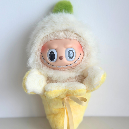 Labubu doll wearing banana costume with white fuzzy hood representing peeled banana top and yellow fuzzy body with ribbon tie - cute fruit-themed doll outfit
