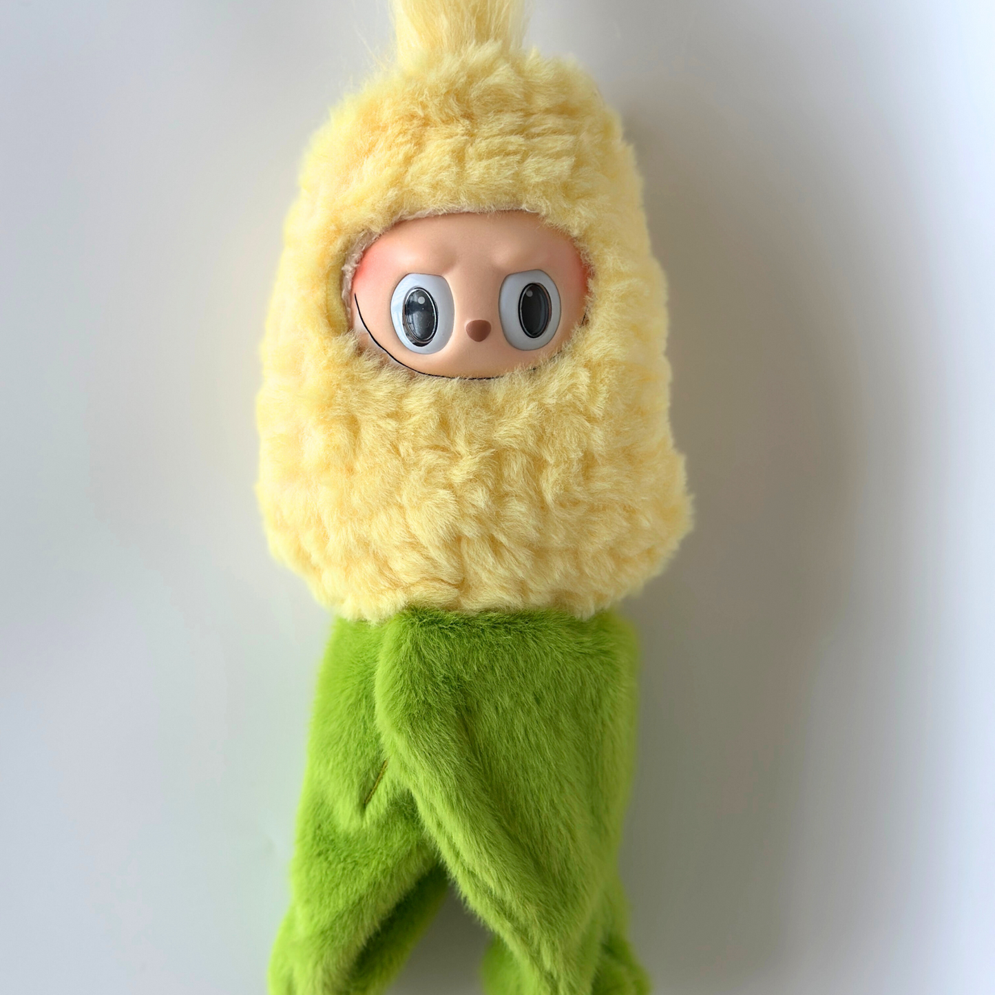 Front view of Labubu doll in corn costume standing upright with yellow fuzzy corn kernels hood and green plush corn husk wrap around lower body - adorable vegetable-themed doll outfit