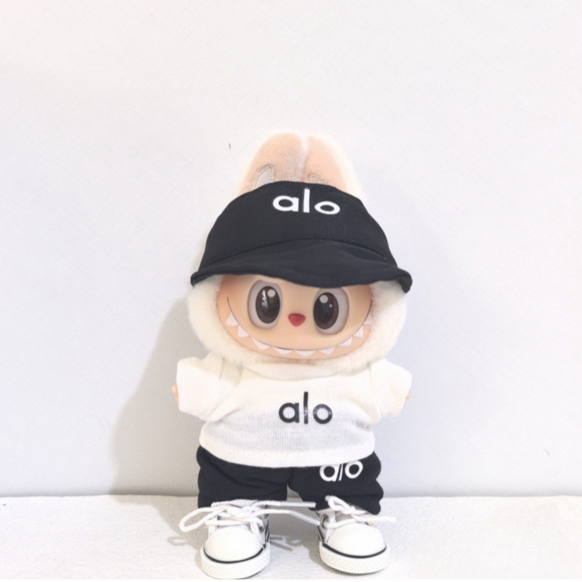Cute labubu dolll in alo sportswear outfit with black cap, white hoodie, black shorts and matching white sneakers