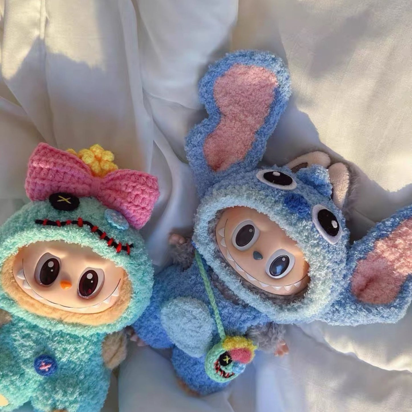 Two labubu  dolls, one blue and one green, with large eyes and colorful accents wearing sitch outfit in a white background.