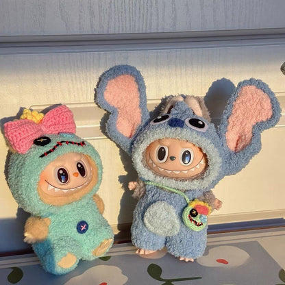 Two labubu dolls one in a green outfit with a pink bow and the other in a blue stitch outfit, on a light-colored surface.