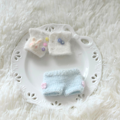 Knitted labubu outfit with top and pants on a white lace plate against a white textured background