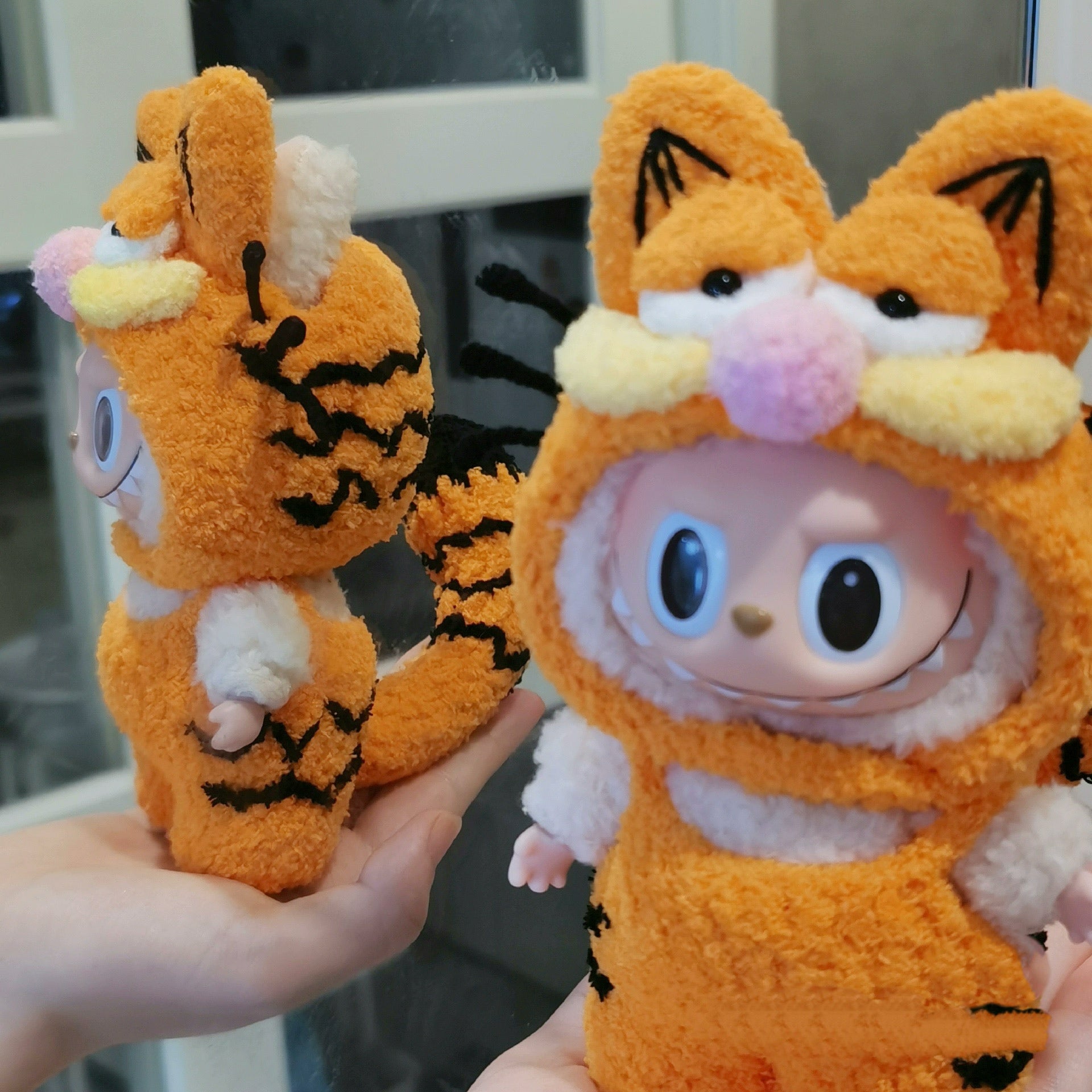 Labubu doll wearing a handmade Garfield-style orange plush outfit with cat ears and whiskers, cute fluffy costume inspired by Garfield.