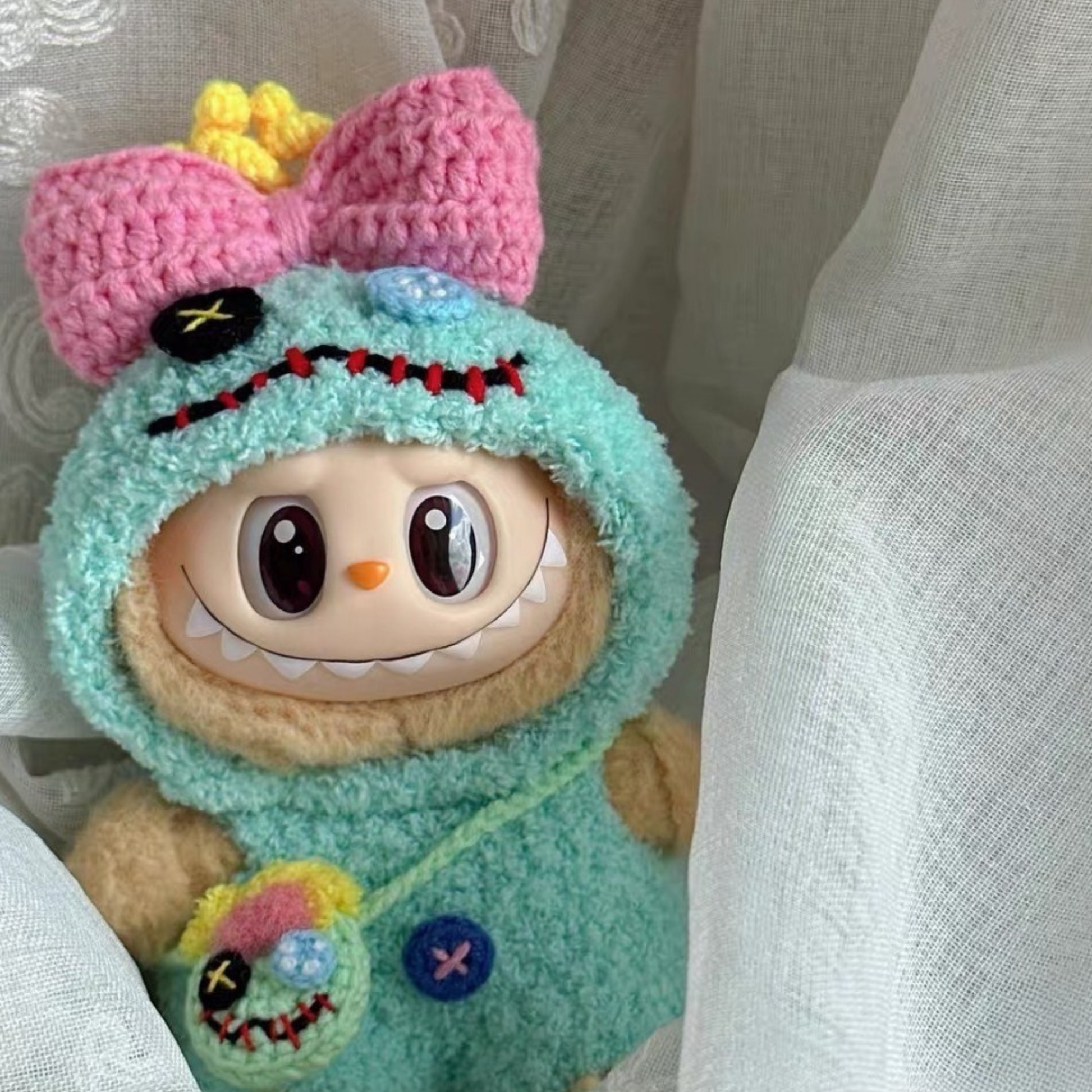 Labubu doll wearing handmade teal crochet Scrump costume with pink bow