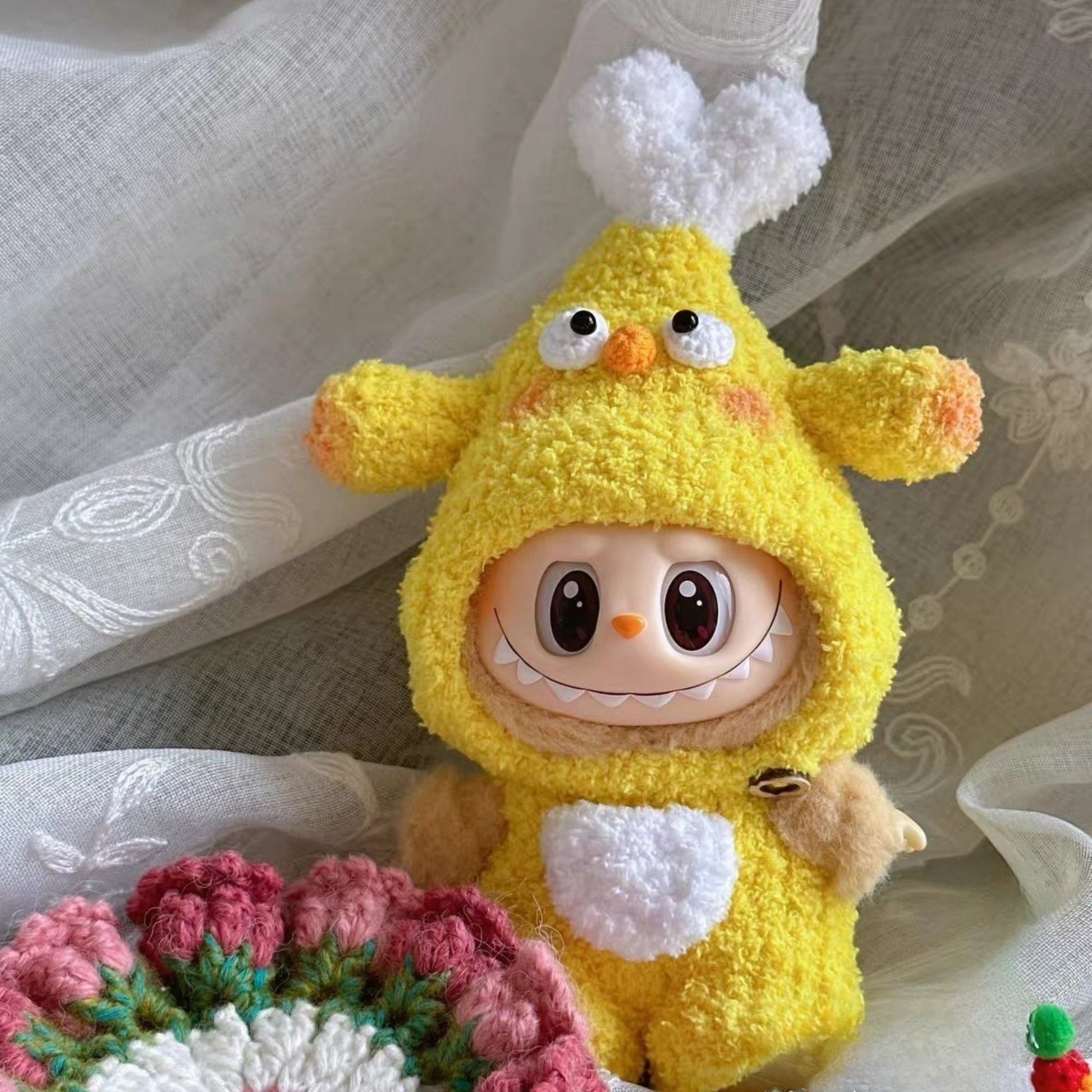 Handmade yellow chicken drumstick outfit for Labubu doll with fluffy white wing details and orange textured accents, photographed lying flat on delicate white lace fabric surrounded by crocheted daisy flowers and pearl strand accessories