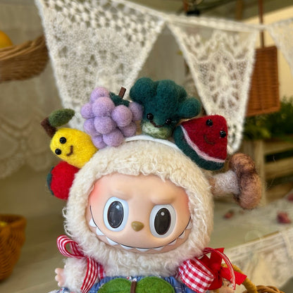 Close-up detail of Labubu doll wearing handmade felt fruit crown headband featuring cute yellow lemon with black bead eyes, purple grapes cluster, green broccoli, red watermelon slice with black seeds, and brown pretzel decoration. Set against white lace curtain backdrop with soft natural lighting, showcasing intricate craftsmanship of miniature fruit accessories for collectible doll costume.