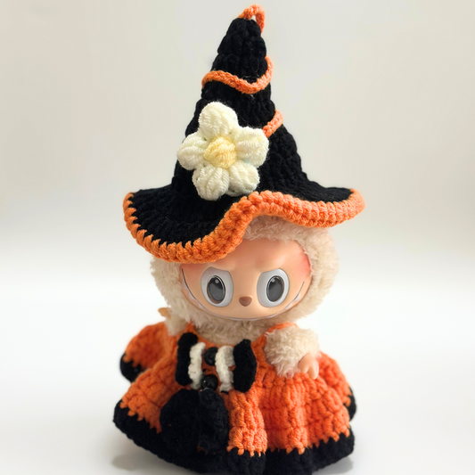 Labubu doll wearing handmade crocheted Halloween witch costume featuring black pointed hat with orange trim, pom-pom, and white daisy flower decoration, plus orange textured dress with black trim details and matching accessories. Adorable Halloween doll outfit with floral embellishment, perfect collectible seasonal costume for toy enthusiasts and craft lovers.