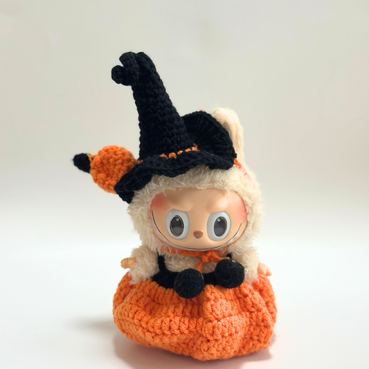 Single Labubu doll wearing handmade crocheted Halloween witch costume featuring black pointed hat with orange pom-pom trim, orange textured pumpkin dress with ribbed pattern, and black accessories including small bag. Adorable Halloween doll portrait, collectible seasonal costume perfect for toy photography and doll enthusiasts.