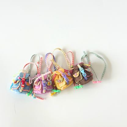 Collection of handmade miniature backpacks for Labubu dolls in various corduroy fabrics including blue, purple, yellow, and brown, each featuring colorful rainbow straps, metal buckle details, front pockets, and decorative ribbon accessories with small charms. Shows variety of color options and intricate craftsmanship of doll backpack accessories, perfect for collectors seeking multiple options.
