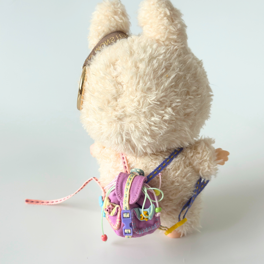 Back view of Labubu doll wearing miniature colorful backpack with purple cotton fabric, rainbow straps in pink, blue, yellow and green, metal buckle details, and various decorative ribbons and charms. Shows intricate craftsmanship of handmade doll accessory with realistic backpack design and functional straps, perfect collectible item for toy enthusiasts.