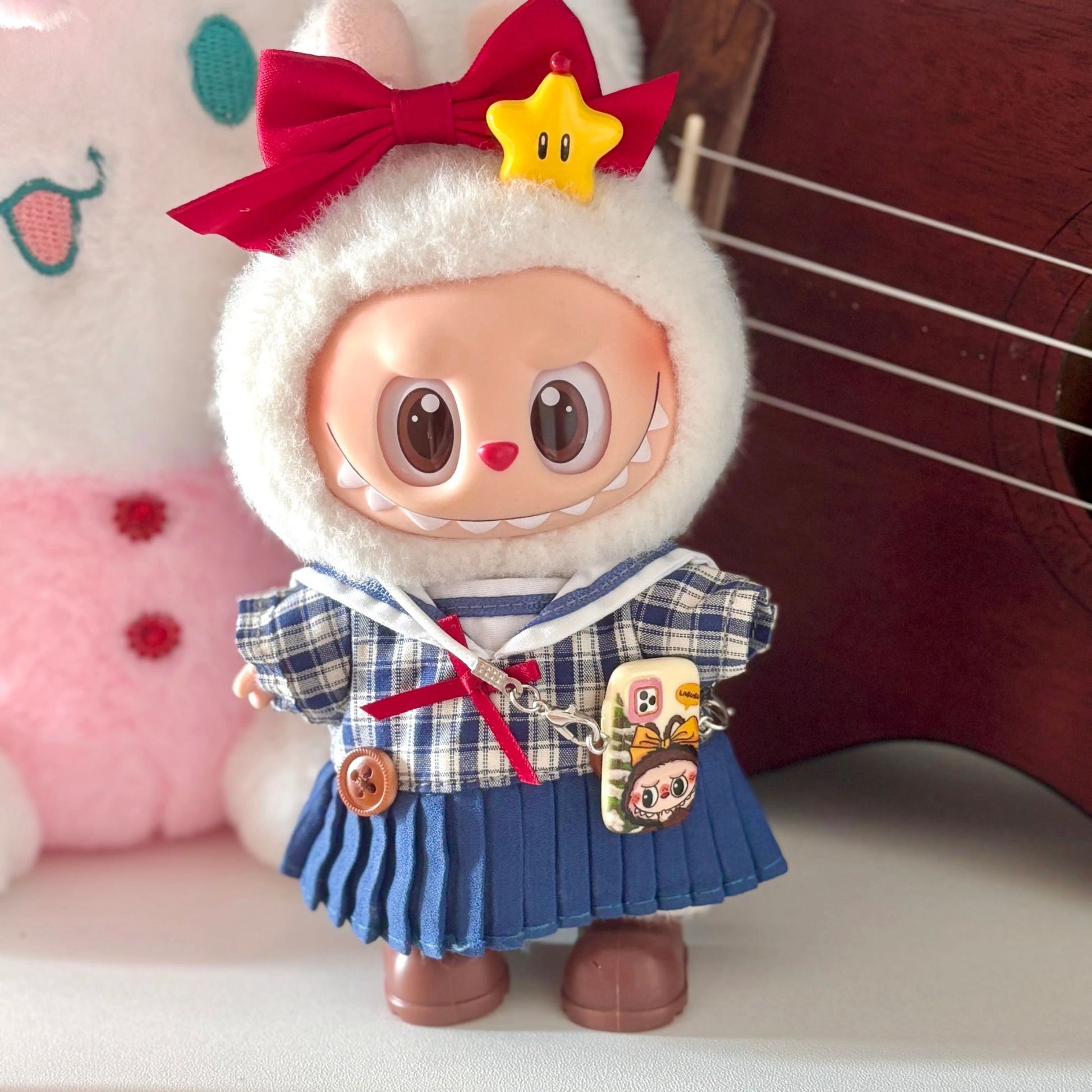 Labubu doll wearing handmade Japanese school uniform costume featuring navy and white plaid sailor-style top with white collar, blue pleated skirt with suspender straps, red bow tie and matching hair bow, yellow star hair clip, and character charm accessories. Perfect academic-themed doll outfit for kawaii fashion collectors and Japanese culture enthusiasts.