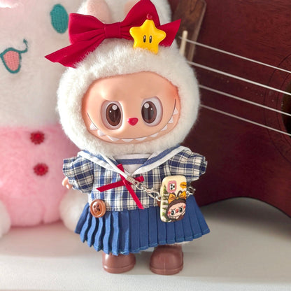 Labubu doll wearing handmade Japanese school uniform costume featuring navy and white plaid sailor-style top with white collar, blue pleated skirt with suspender straps, red bow tie and matching hair bow, yellow star hair clip, and character charm accessories. Perfect academic-themed doll outfit for kawaii fashion collectors and Japanese culture enthusiasts.